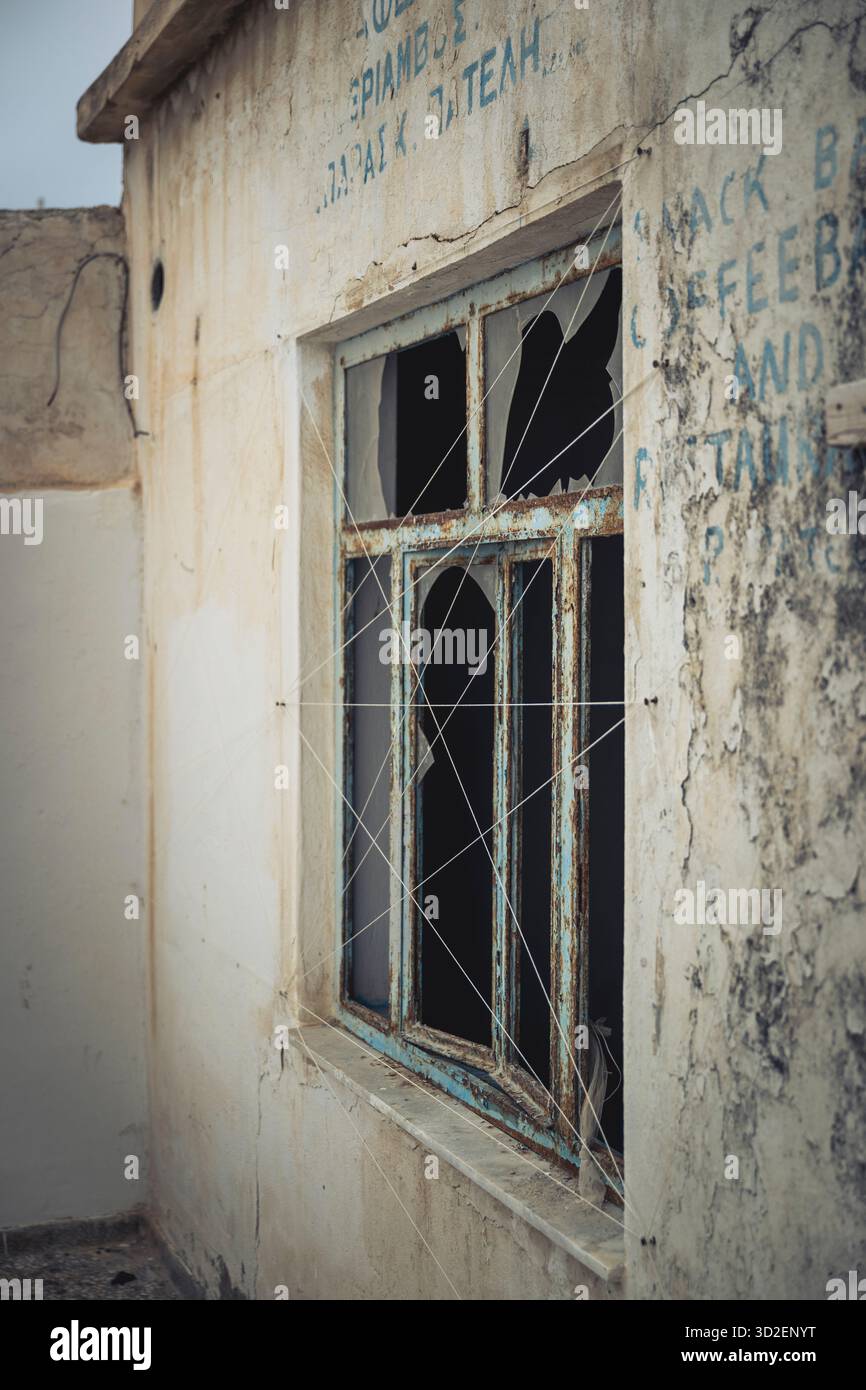 Une fenêtre cassée d'un ancien café dans un bâtiment abandonné dans la vieille ville de Marpissa, Paros, Grèce Banque D'Images