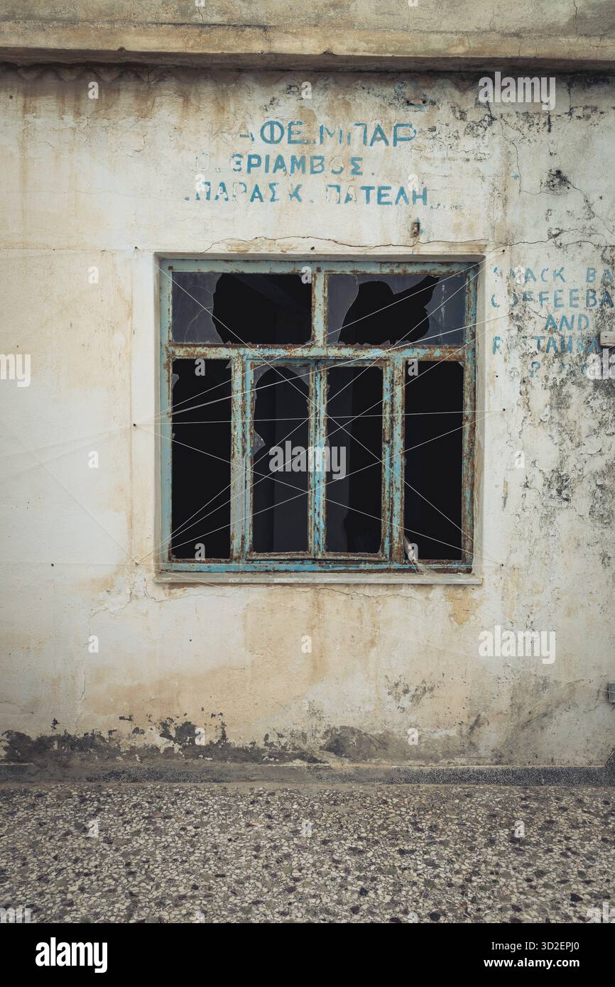 Une fenêtre cassée d'un ancien café dans un bâtiment abandonné dans la vieille ville de Marpissa, Paros, Grèce Banque D'Images