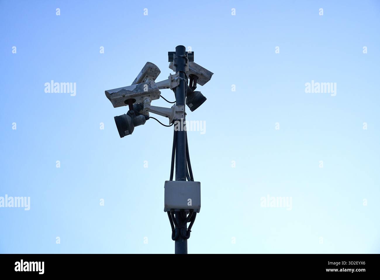 Un groupe de caméras de surveillance montées sur un poteau, pointant dans différentes directions, contre un ciel bleu clair. Banque D'Images
