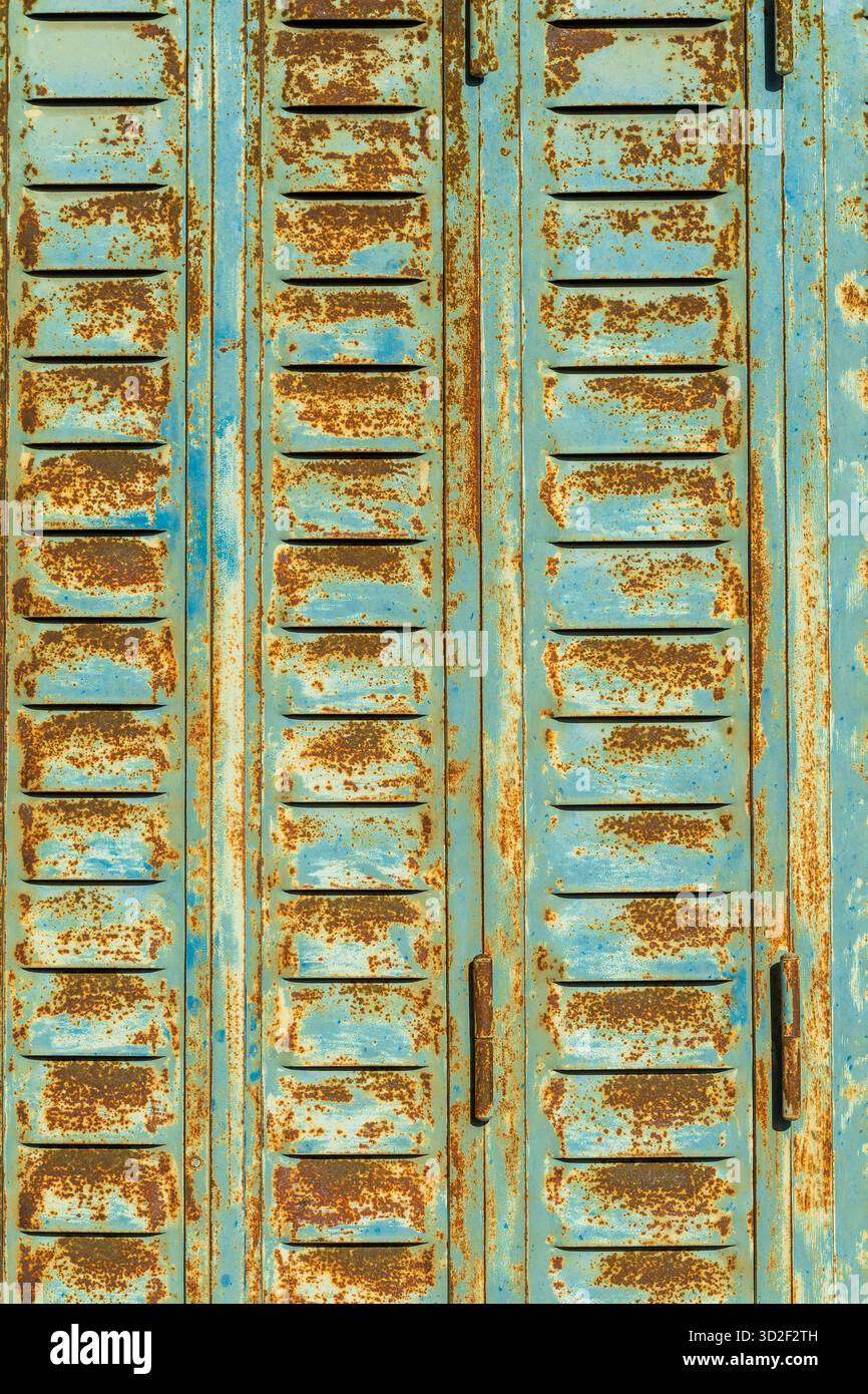 Vieux volet métallique bleu avec évents montre la rouille et les ombres d'arbres par une journée ensoleillée Banque D'Images