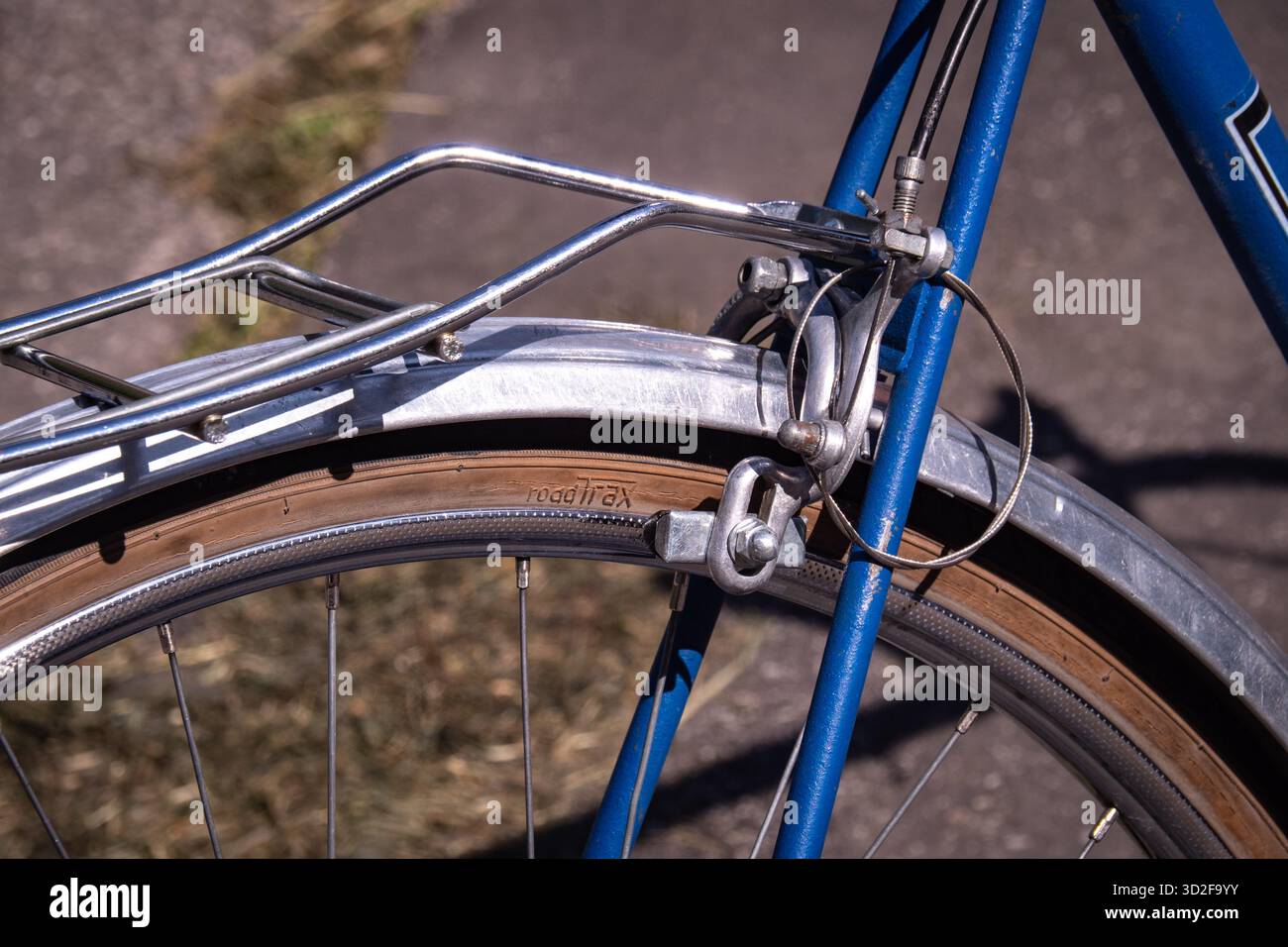 Détail en gros plan de la roue arrière, de la crémaillère et du mécanisme de freinage d'un vélo bleu vintage garé à l'extérieur. Banque D'Images
