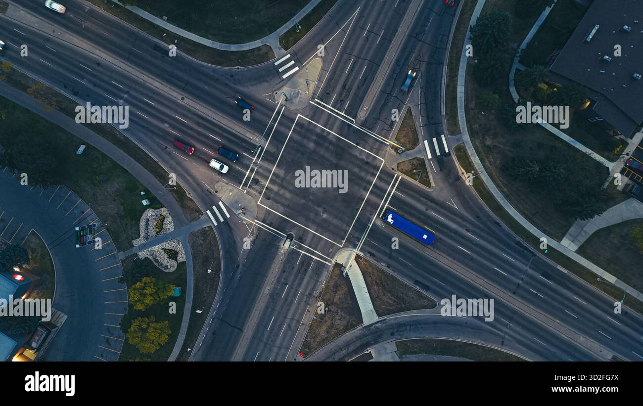 Vue drone des feux de circulation illuminés et des voitures à une grande intersection dans la soirée. Banque D'Images