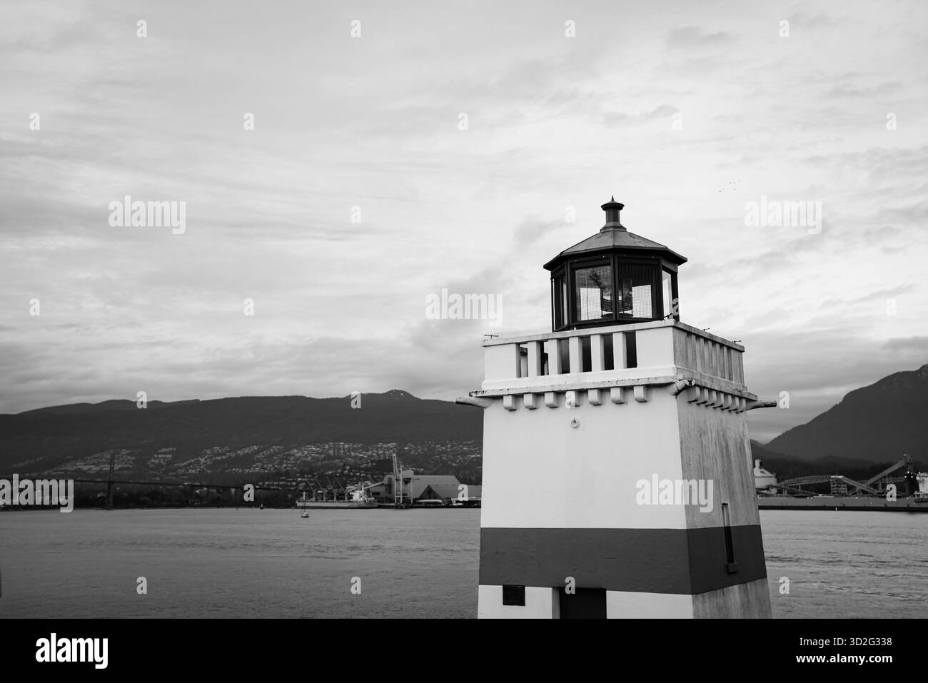 Image en noir et blanc du phare de Brockton point surplombant Burrard Inlet, encadré par les montagnes de la rive nord et le paysage du port industriel. Banque D'Images