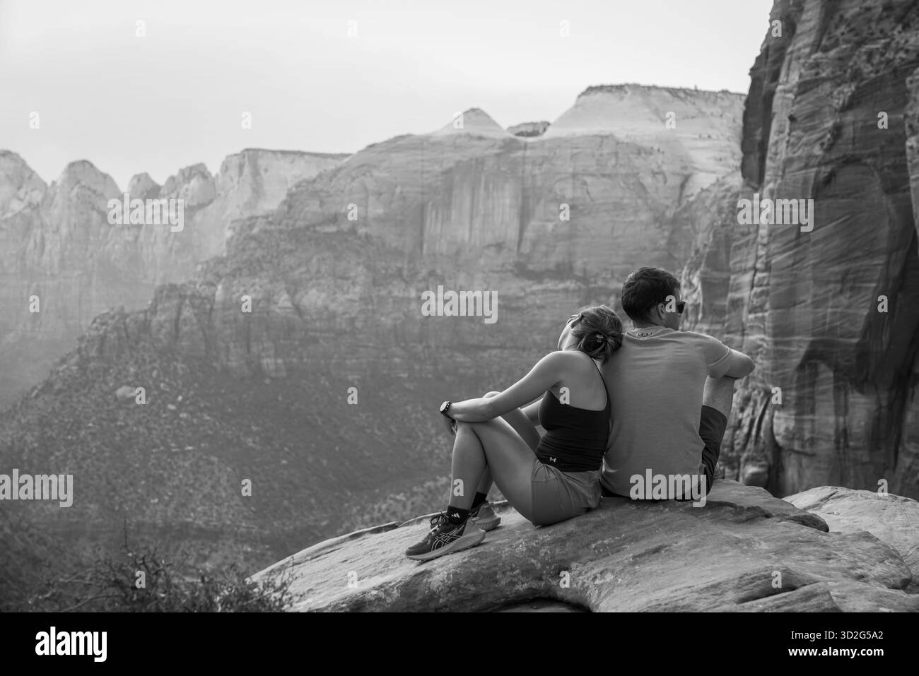 Un couple se penche ensemble sur une falaise près d’Angel’s Landing dans cette vue en noir et blanc du paysage spectaculaire du canyon. Banque D'Images