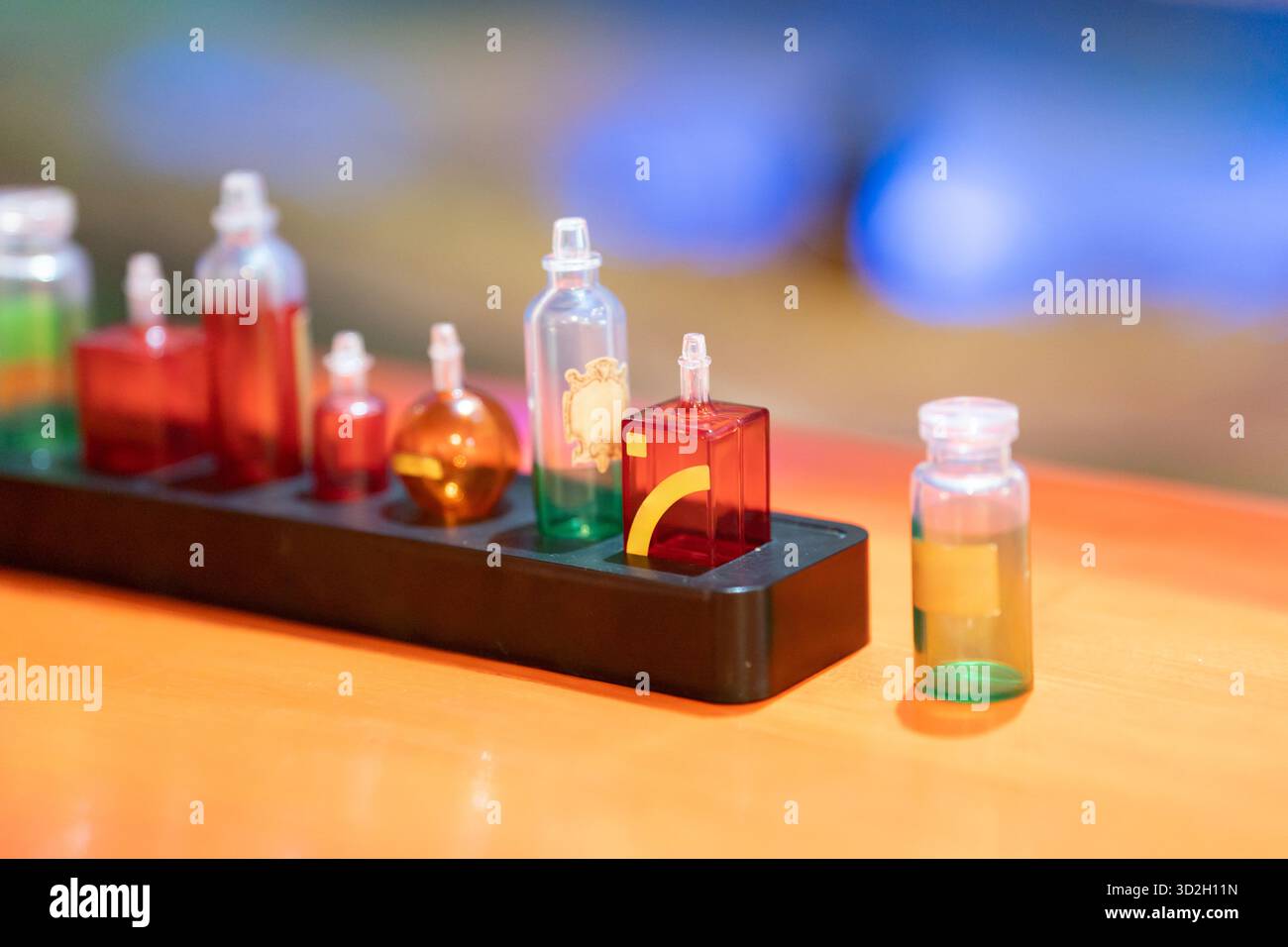 Une rangée de petites bouteilles en verre remplies de liquides brillants se trouve sur un rack en plastique noir, créant une scène de laboratoire vibrante parfaite pour les sciences, la chimie et les visuels de l'éducation. Photo de haute qualité Banque D'Images