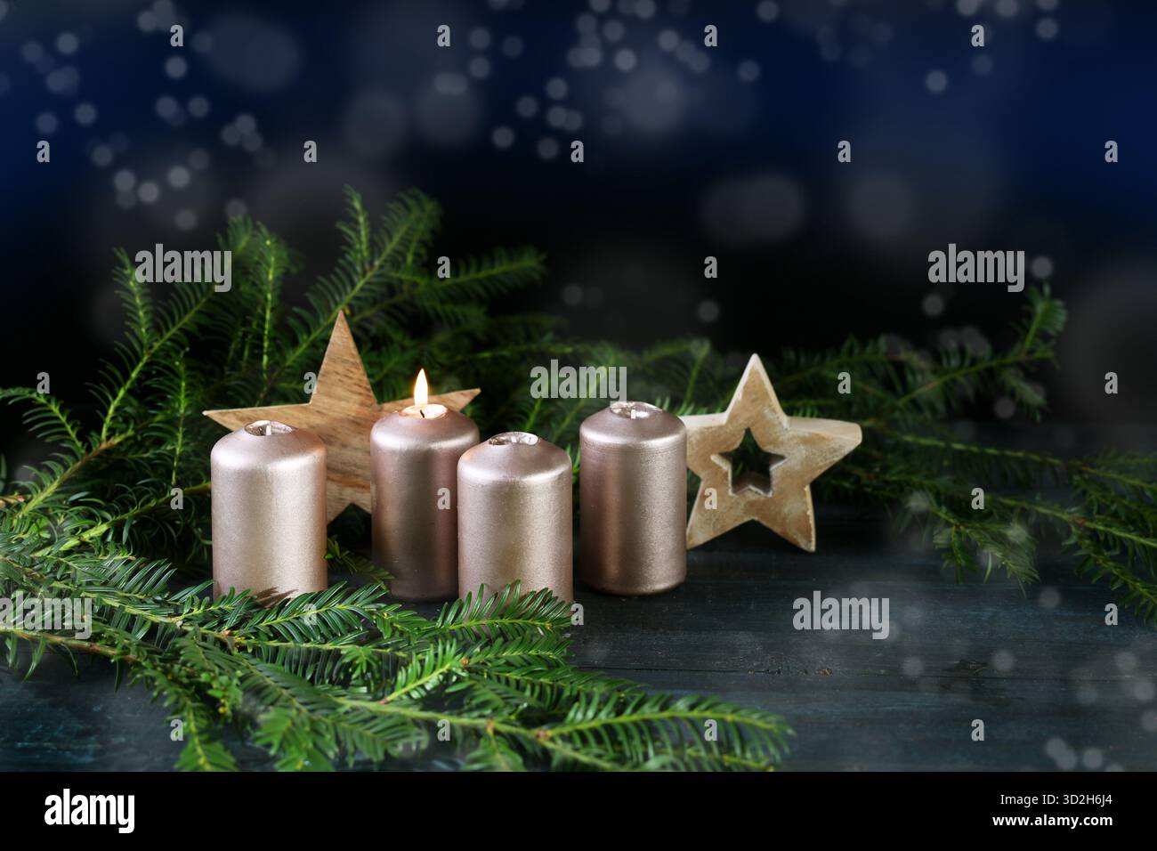 Quatre bougies dorées, une allumée pour le premier Avent, étoiles en bois et branches de sapin sur un fond sombre avec bokeh enneigé, vacances d'hiver, copie Banque D'Images