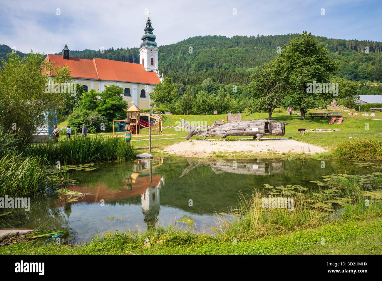 Engelhartszell, Autriche - 1er juillet 2019 : structure de jeu d'esturgeon béluga en bois et abbaye d'Engelszell reflétée dans l'étang. Banque D'Images