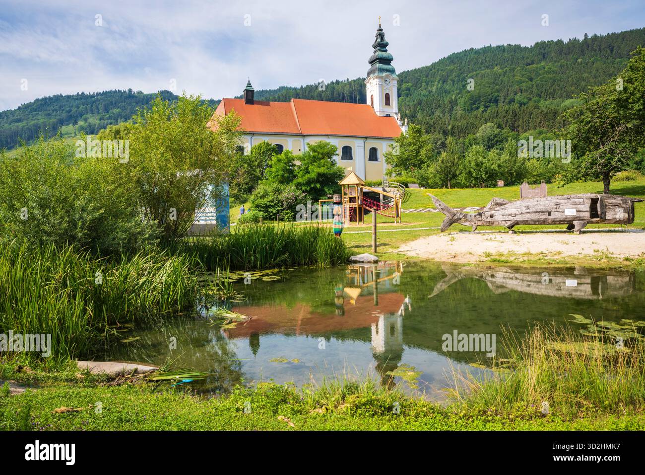 Engelhartszell, Autriche - 1er juillet 2019 : structure de jeu d'esturgeon béluga en bois et abbaye d'Engelszell reflétée dans l'étang. Banque D'Images