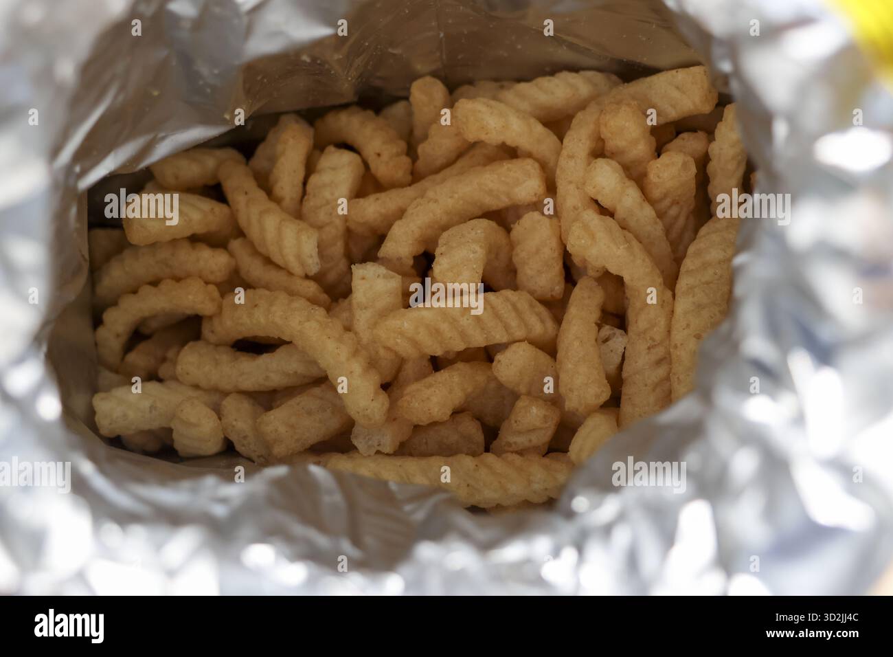 Vue rapprochée satisfaisante regardant à l'intérieur d'un sac en aluminium ouvert rempli d'en-cas jaune croquant. Cette délicieuse malbouffe striée offre une friandise salée pour mun Banque D'Images