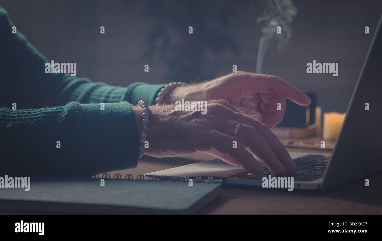 Inspiration tranquille. Les mains tournent les pages du carnet près de la lueur de l'ordinateur, scène baignée de tons ambres chauds - paisible, cinématographique, vivante Banque D'Images