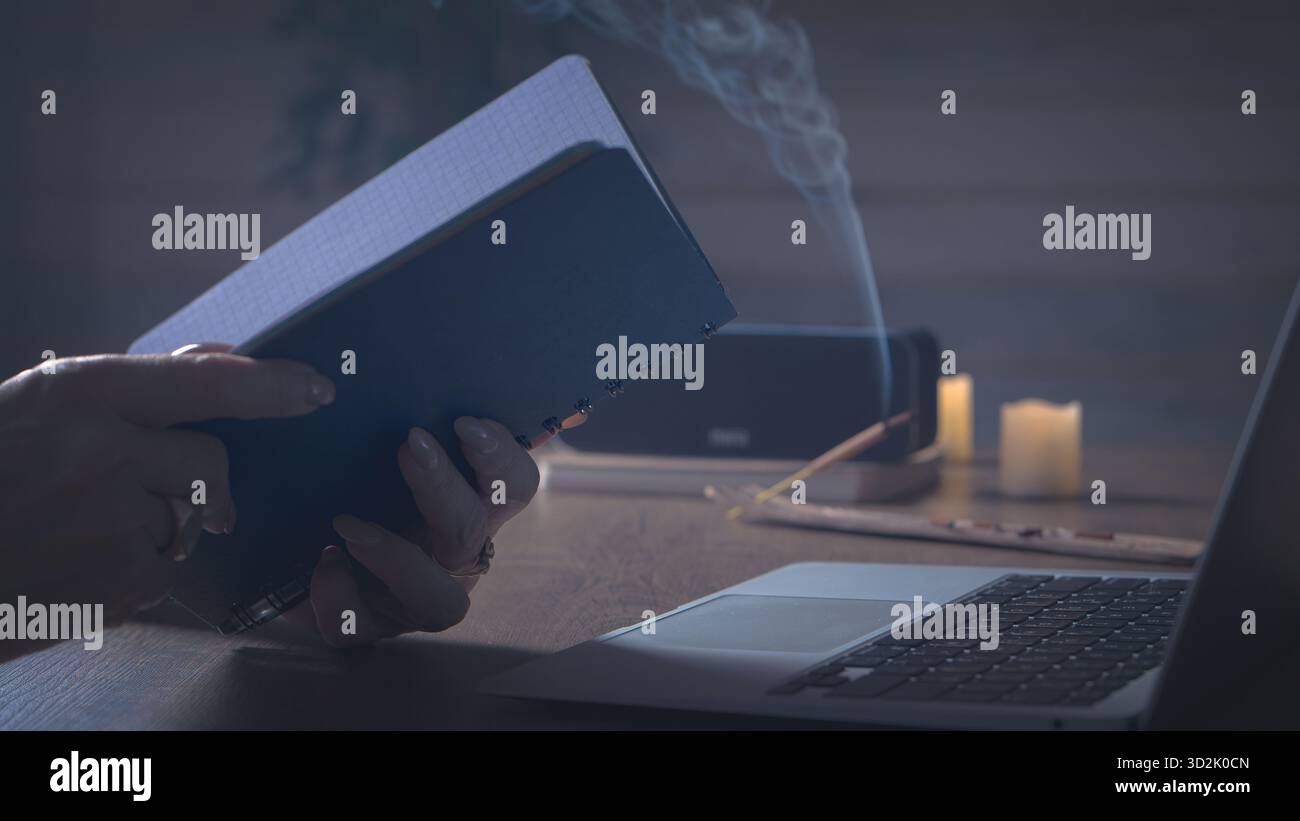 Le calme du soir. Une paire de mains réfléchies pliées près d'un ordinateur de bureau, la lumière ambre et la brume d'encens créent une ambiance de réflexion douce Banque D'Images
