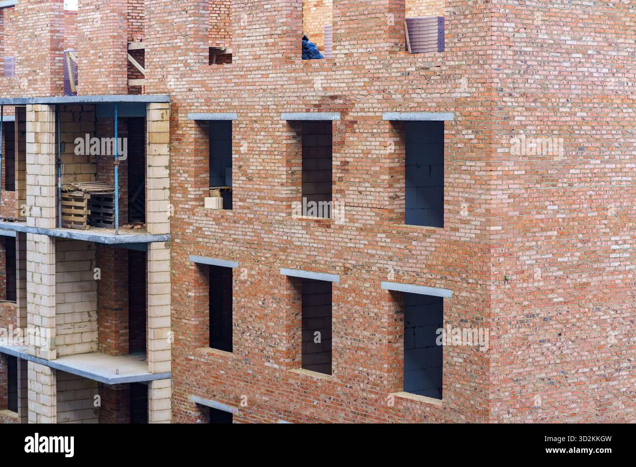 Les ouvriers sont vus sur les niveaux supérieurs d'un bâtiment en brique en construction, avec des cadres de fenêtres et des murs visibles presque achevés. Banque D'Images
