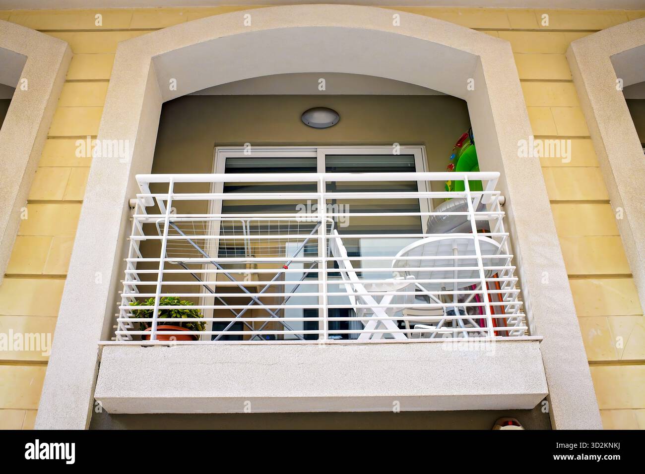 Façade d'une maison avec un petit appartement moderne voûté balcon avec balustrades blanches, meubles, un sèche-linge, et une plante en pot par une journée ensoleillée Banque D'Images
