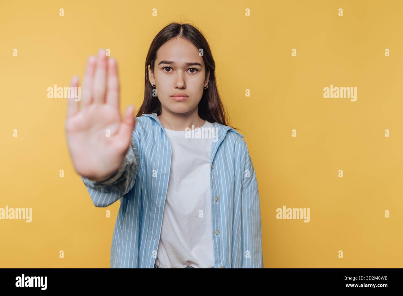 Jeune femme faisant un geste d'arrêt sur fond jaune. Banque D'Images