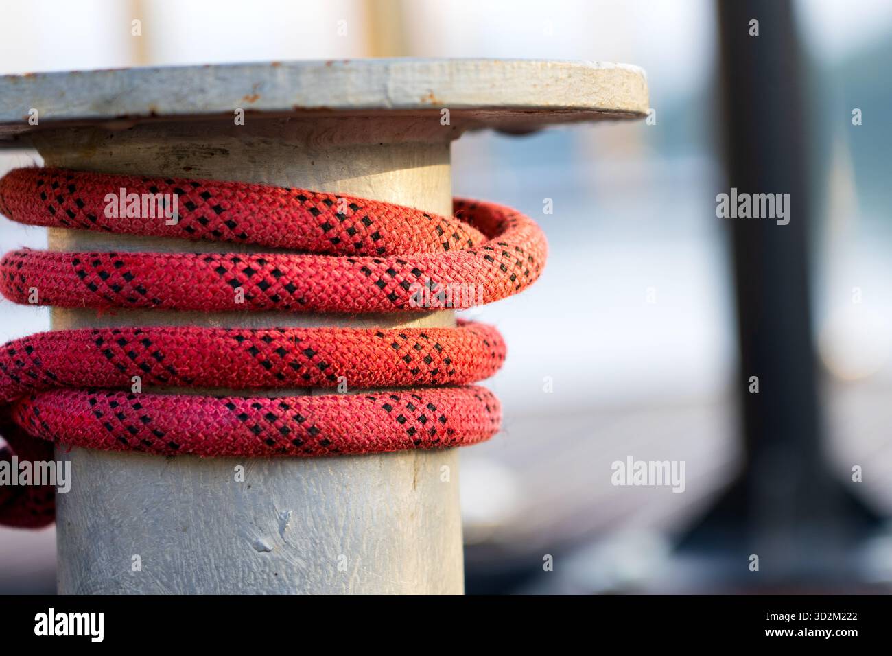 Borne en métal sur quai en bois avec corde rouge solidement enveloppée, attachant un bateau dans un cadre rustique Marina avec fond doux Banque D'Images