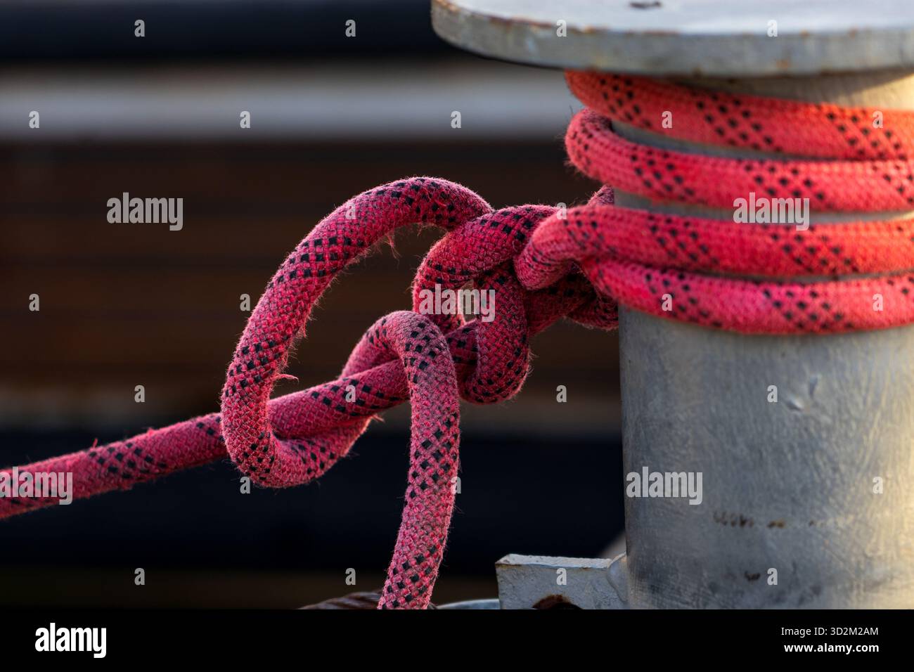 Borne en métal sur quai en bois avec corde rouge solidement enveloppée, attachant un bateau dans un cadre rustique Marina avec fond doux Banque D'Images