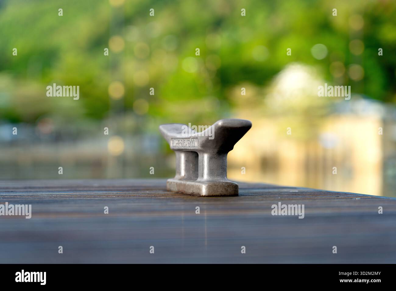 Cale d'amarrage en métal sur un quai en bois, vieilli et altéré, placé sur un fond vert flou avec des lumières bokeh douces Banque D'Images