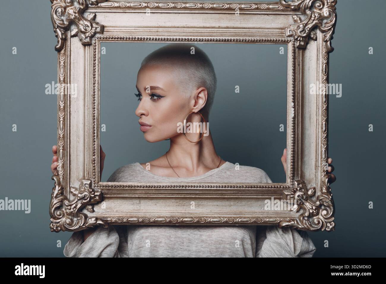 Jeune femme millénaire aux cheveux blonds courts tient le cadre doré dans les mains derrière son portrait de profil de visage Banque D'Images