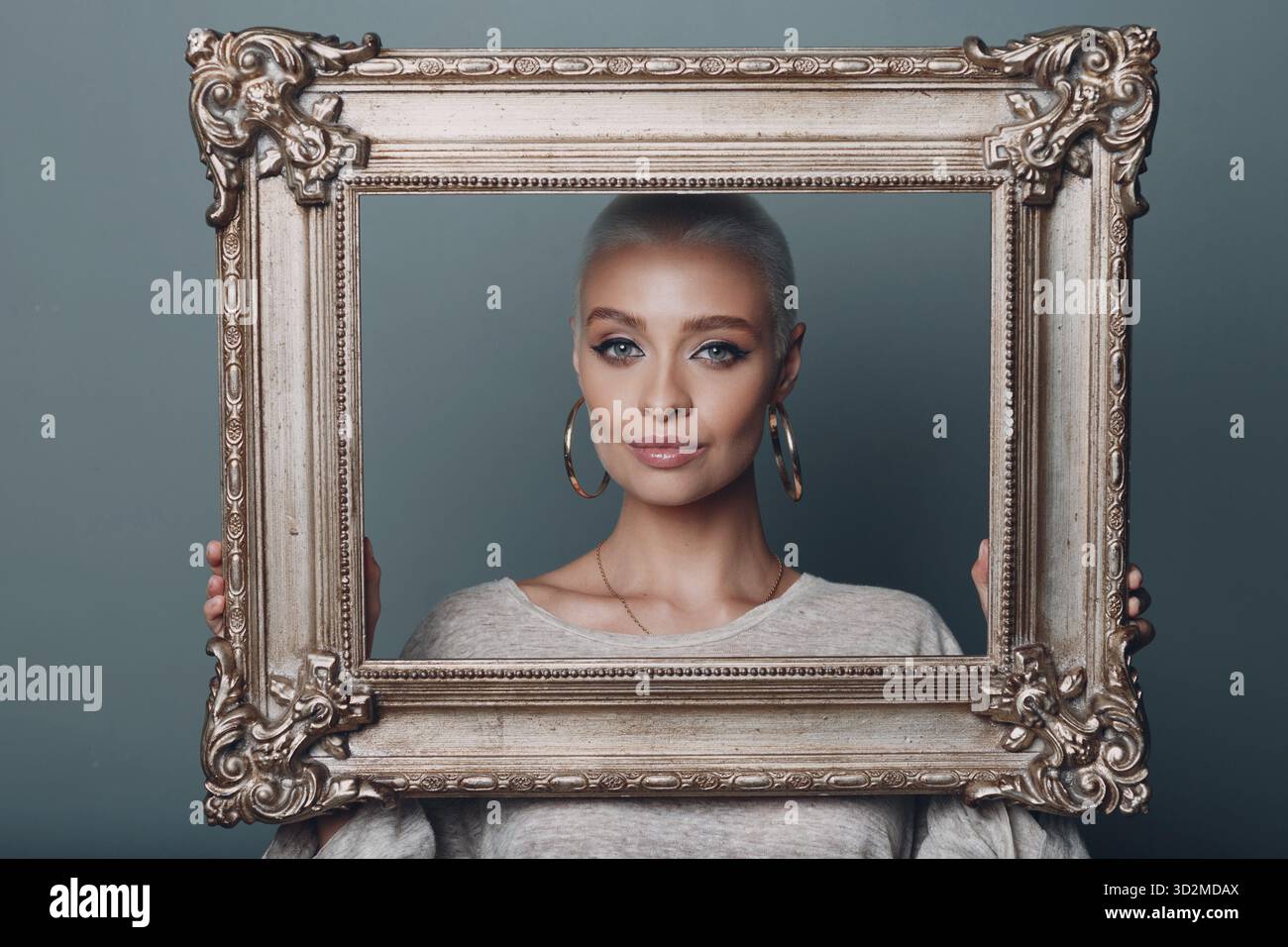 Concept d'atelier de cadrage de baguette. Une fille aux cheveux blonds tient le cadre doré dans les mains derrière son portrait du visage Banque D'Images