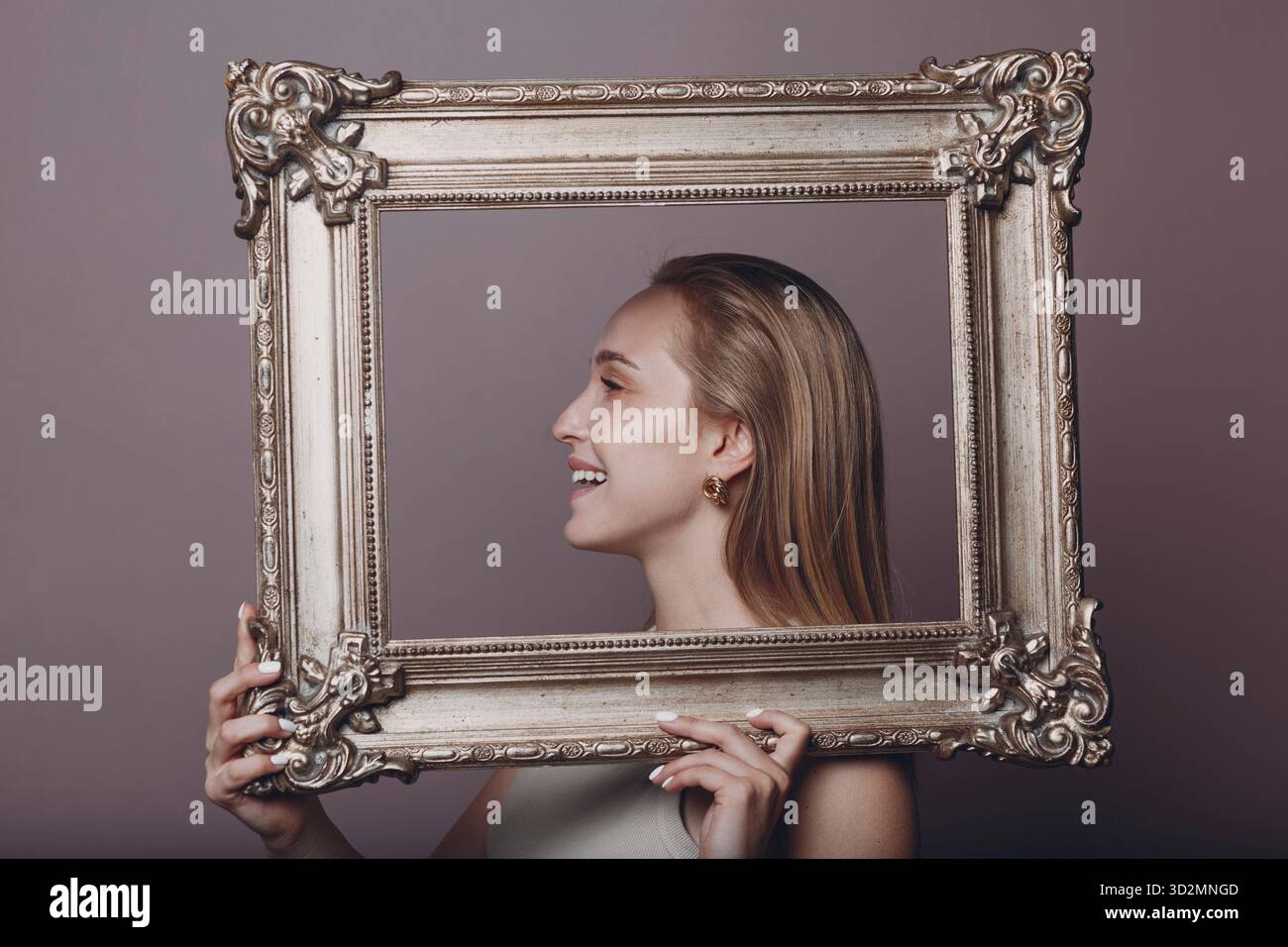 Jeune femme millénial cheveux blonds tient image dorée cadre dans les mains visage portrait Banque D'Images