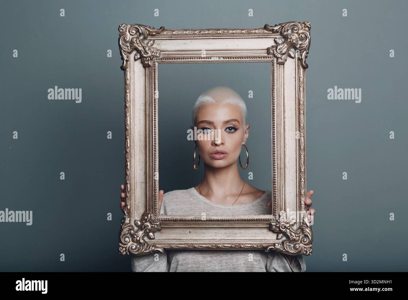 Jeune femme millénaire aux cheveux blonds courts tient le cadre doré dans les mains derrière son portrait du visage Banque D'Images