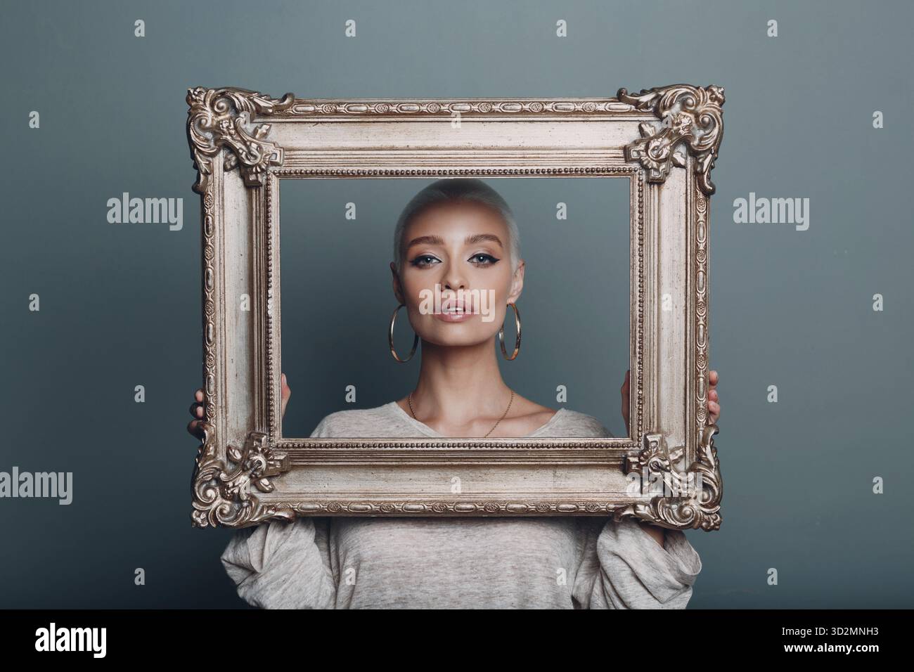 Jeune femme millénaire aux cheveux blonds courts tient le cadre doré dans les mains près de son visage portrait Banque D'Images