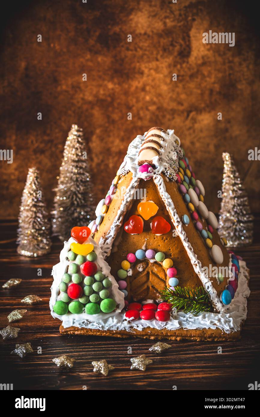 Maison en pain d'épice décorée de bonbons colorés et décoration de noël sur fond de bois, verticale avec espace copie Banque D'Images