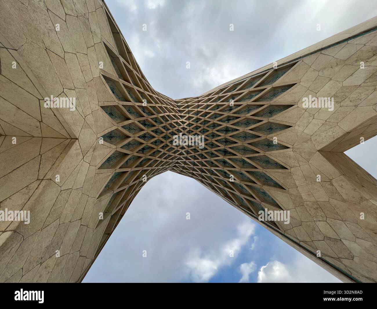 Regardant à travers le treillis géométrique de la Tour Azadi de Téhéran - une fusion emblématique de design persan et moderniste sous un ciel sombre et nuageux. Banque D'Images