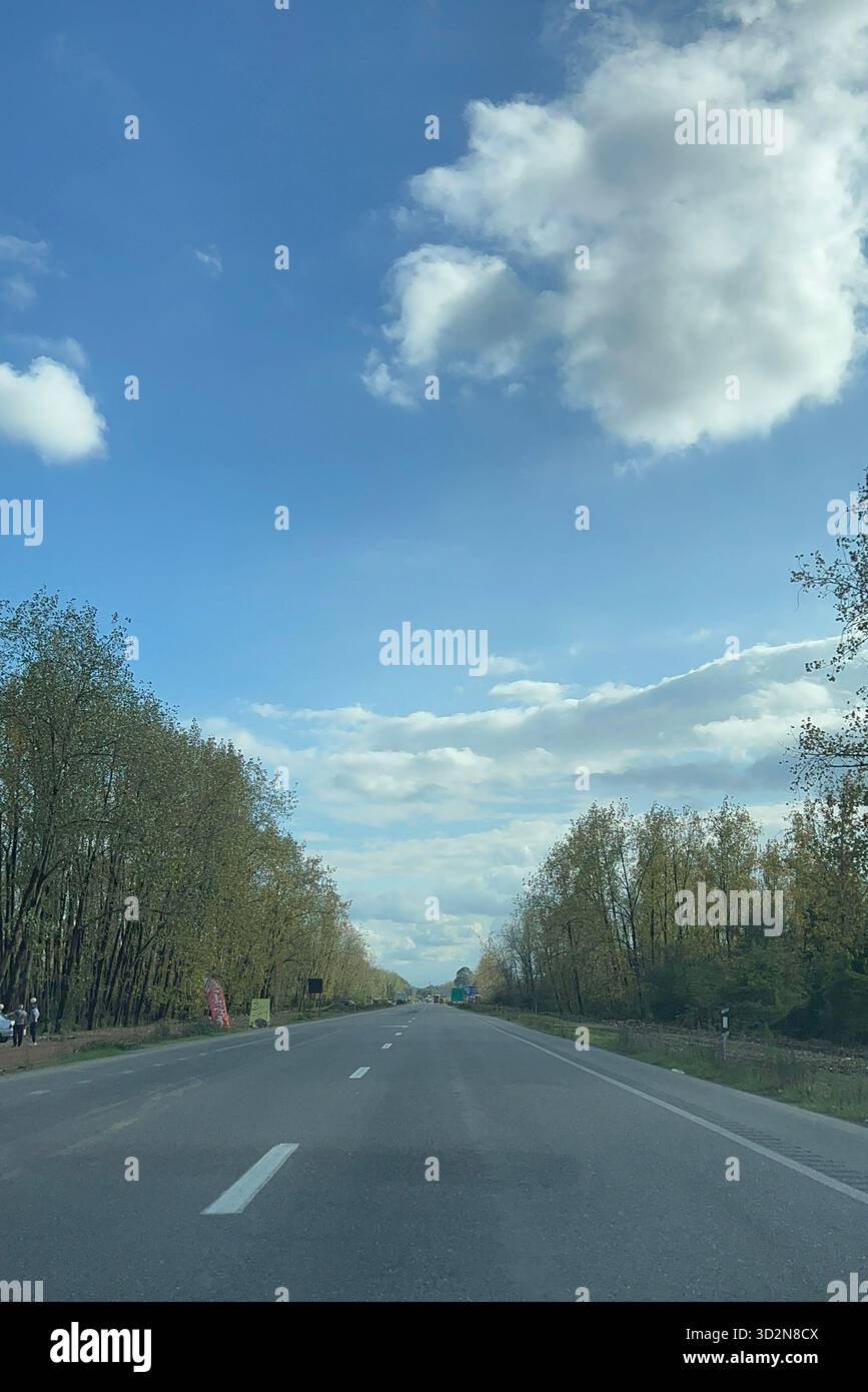 Gilan, Iran — autoroute bordée d'arbres sur la plaine de la Caspienne, longue perspective de point de fuite sous le ciel bleu et les immenses nuages de cumulus. Banque D'Images