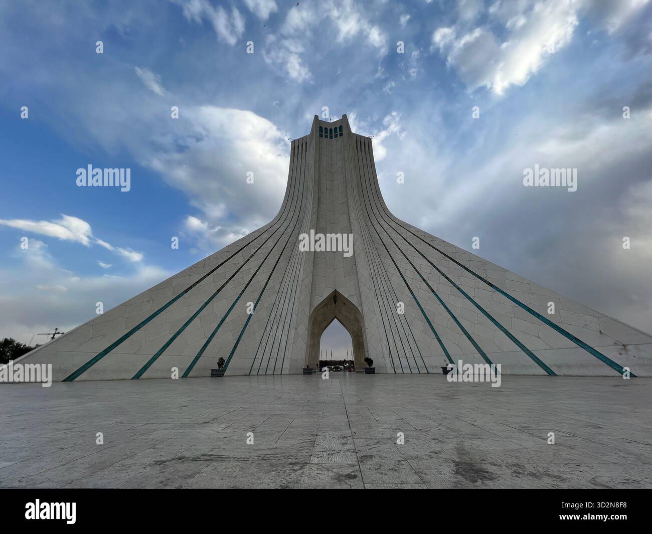 Vue grand angle de la Tour Azadi de Téhéran sous des nuages spectaculaires, des bandes turquoises menant à l'arc central. Banque D'Images