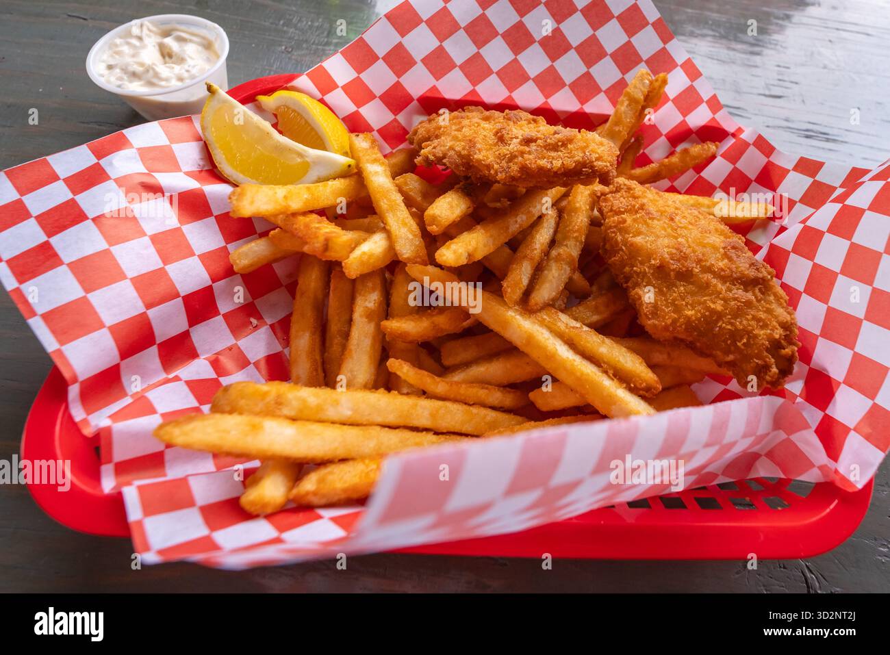 Filets de poisson frits servis avec des frites dorées, des quartiers de citron et de la sauce tartare dans un panier à carreaux doublé de papier. Banque D'Images