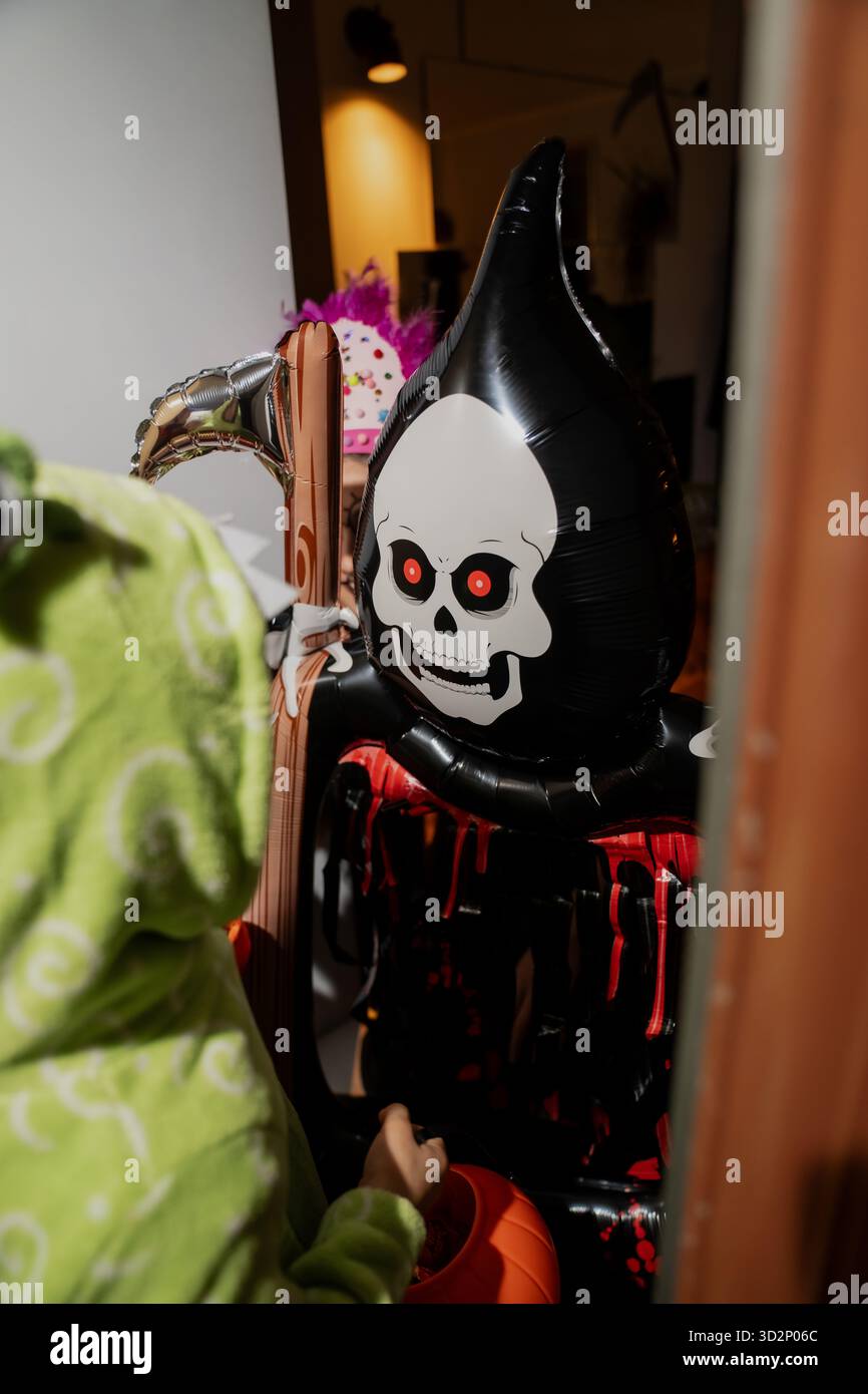 Halloween rencontre de l'enfant dans le costume de pyjama de dinosaure rencontrant la décoration gonflable sinistre faucheuse avec le visage de crâne et les yeux rougeoyants pendant le voisin Banque D'Images