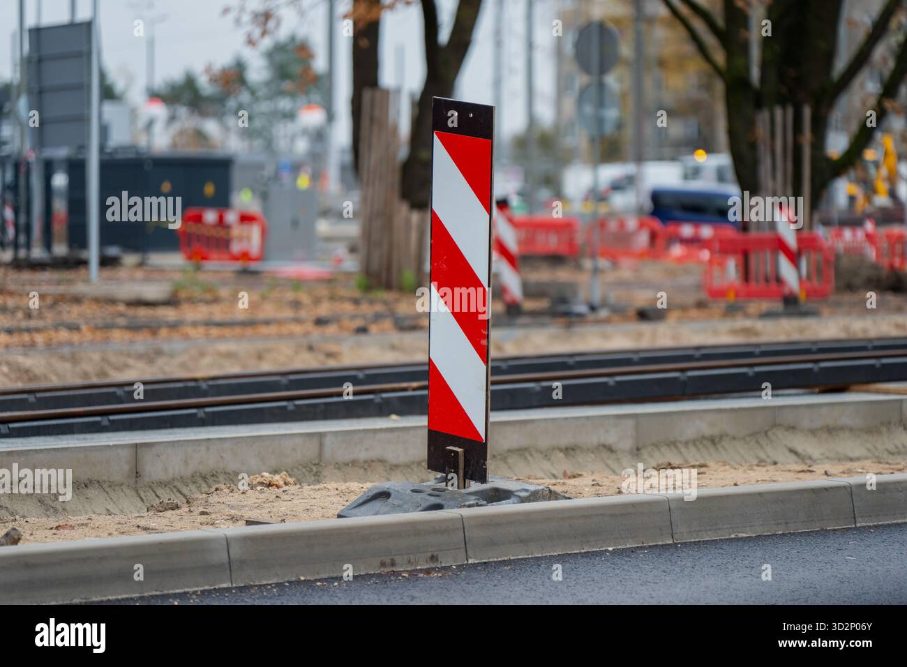 Zone de construction de routes urbaines avec un poste d'avertissement rouge et blanc réfléchissant placé près des voies de tramway et des barrières indiquant la réparation des infrastructures de la ville Banque D'Images