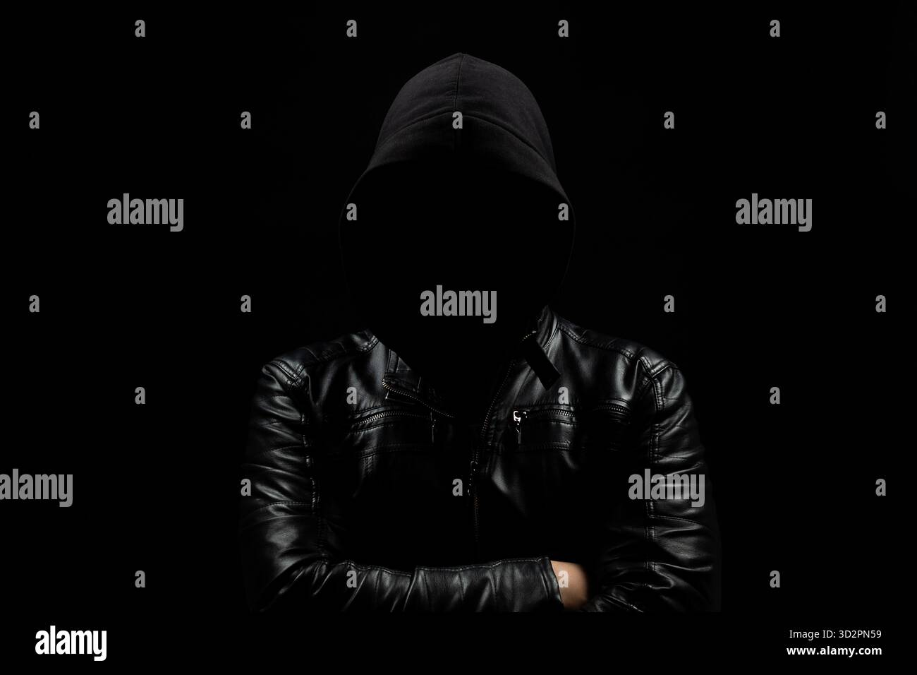 Gros plan sur un homme hacker à capuche sans visage dans l'ombre avec les bras croisés et un fond noir Banque D'Images