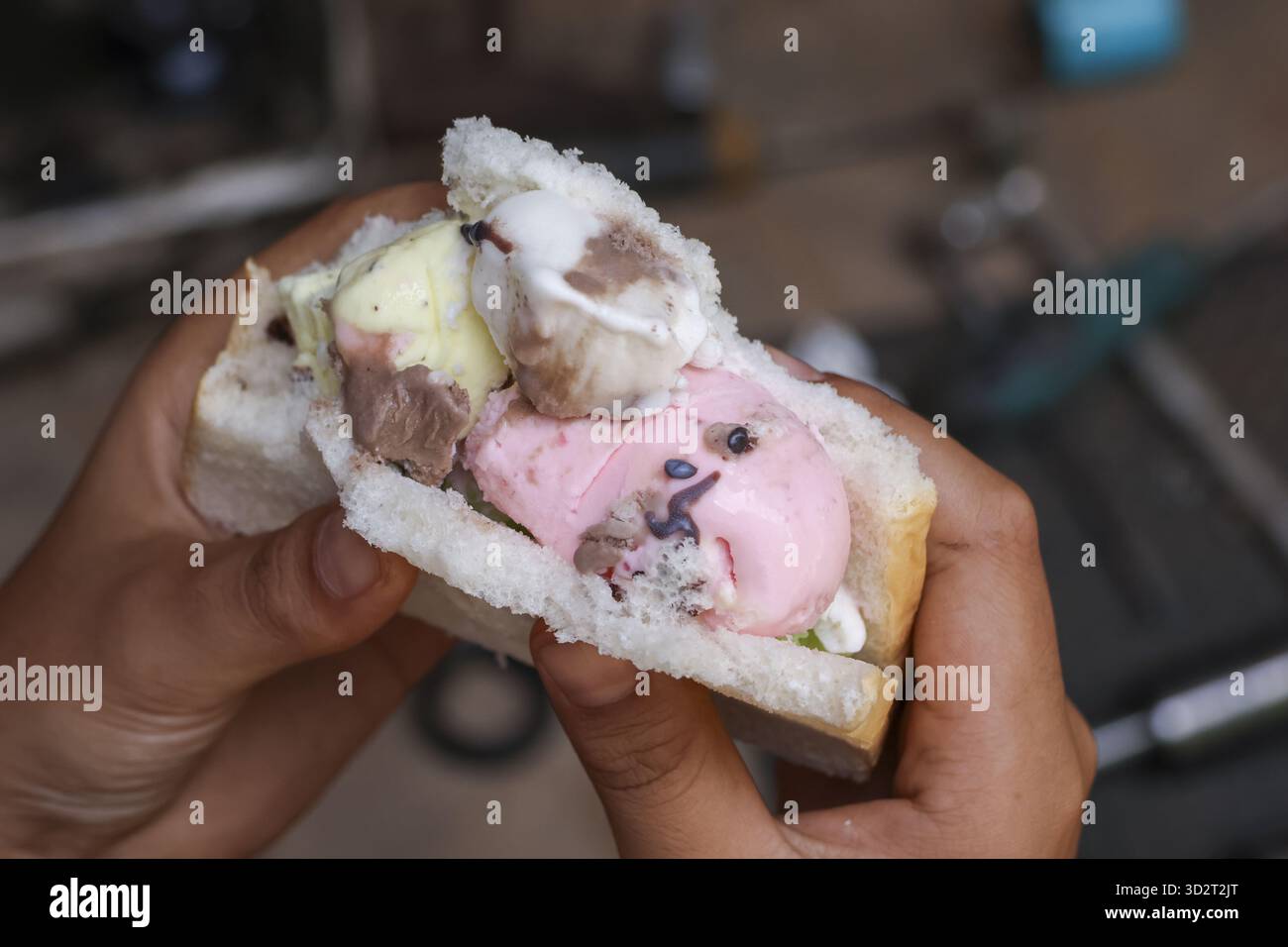 Gros plan de la main tenant un sandwich coloré au pain à la crème glacée, collation populaire de la nourriture de rue. Saveur rafraîchissante de rose, vanille et chocolat pour un gâteau sucré A. Banque D'Images