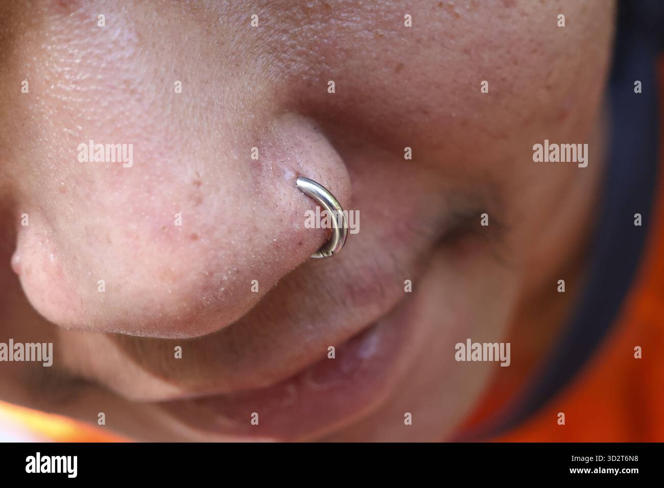 Gros plan du visage de la personne montrant le perçage argenté de l'anneau nasal. l’accent est mis sur la texture de la peau et les bijoux, avec une expression neutre et authentique Banque D'Images