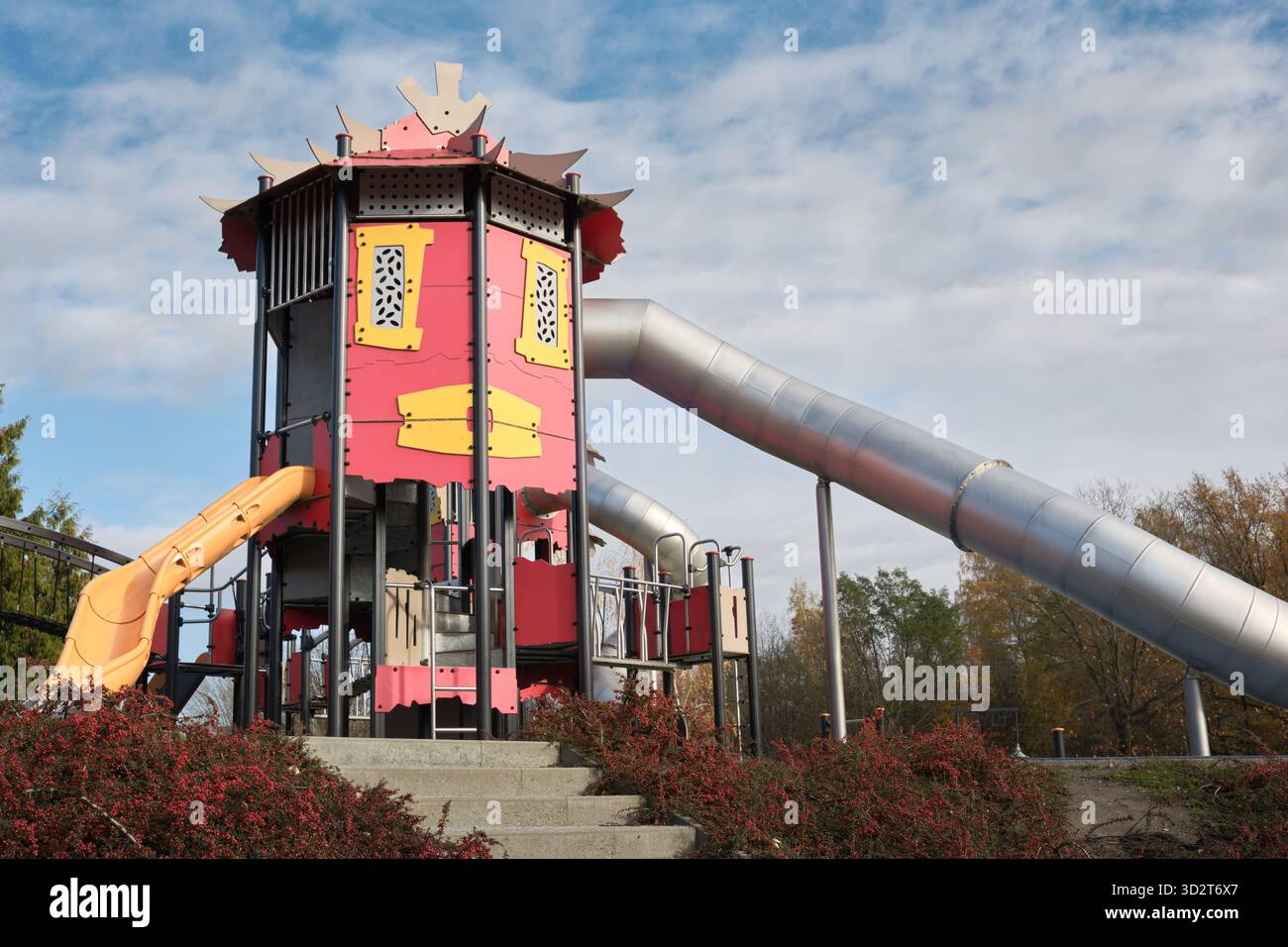 Structure moderne de terrain de jeu rouge avec une longue glissière en métal et des surfaces de sécurité dans un parc urbain à Lodz, en Pologne, conçu pour les loisirs en plein air des enfants. Banque D'Images