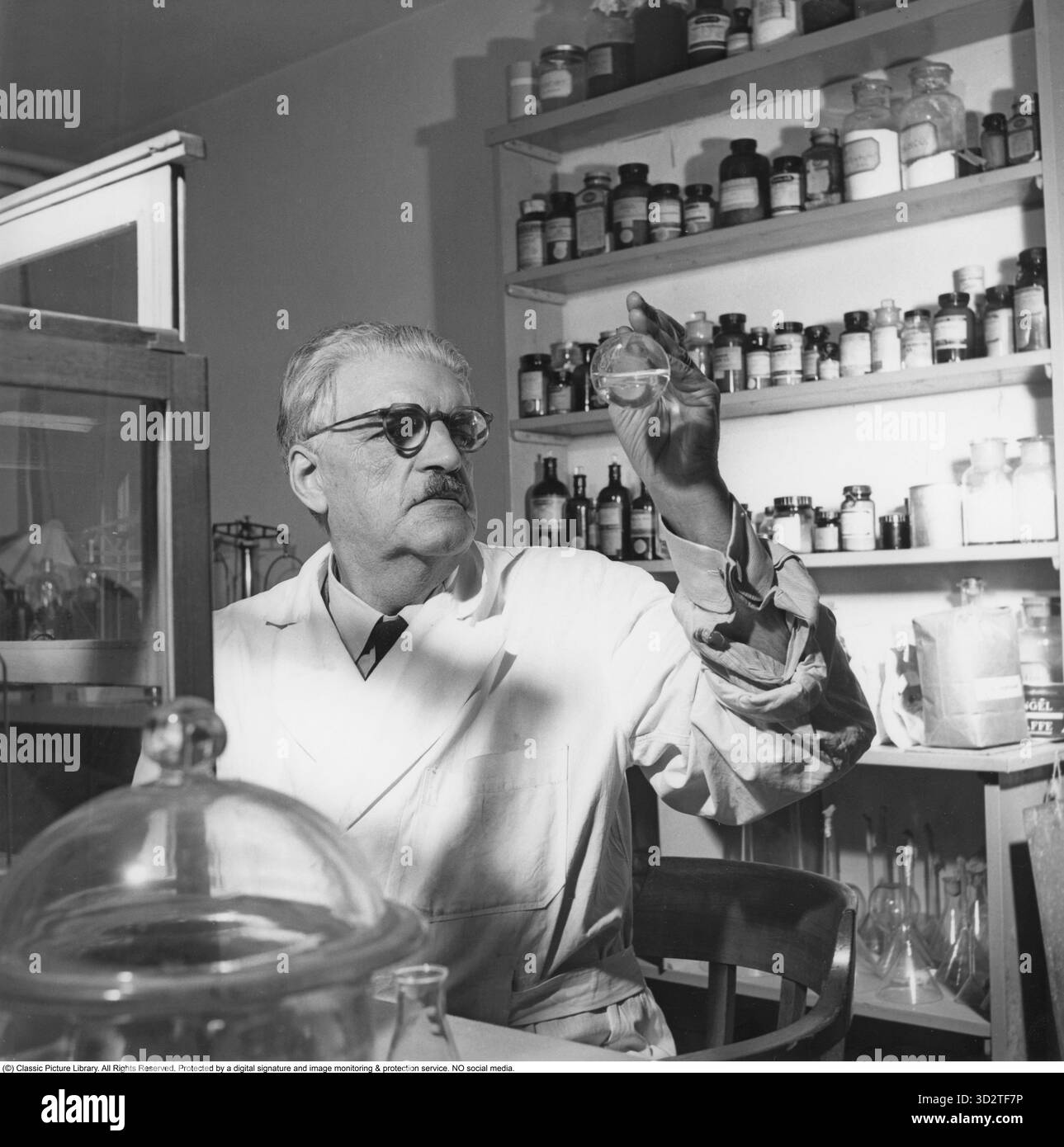 Dans le laboratoire de Stockholm, 1953, Un scientifique examine un tube de verre contenant un échantillon, entouré d'étagères bordées de divers flacons et contenants essentiels pour le travail en laboratoire. Cette image capture l'essence de la recherche scientifique du milieu du XXe siècle en Suède, une période marquée par des avancées significatives en chimie et en sciences médicales. Des laboratoires comme celui-ci ont joué un rôle central dans la stimulation de l’innovation, contribuant à la réputation de la Suède en tant que plaque tournante pour les découvertes scientifiques pendant l’après-guerre. 1953 Conard ref 2490 Banque D'Images