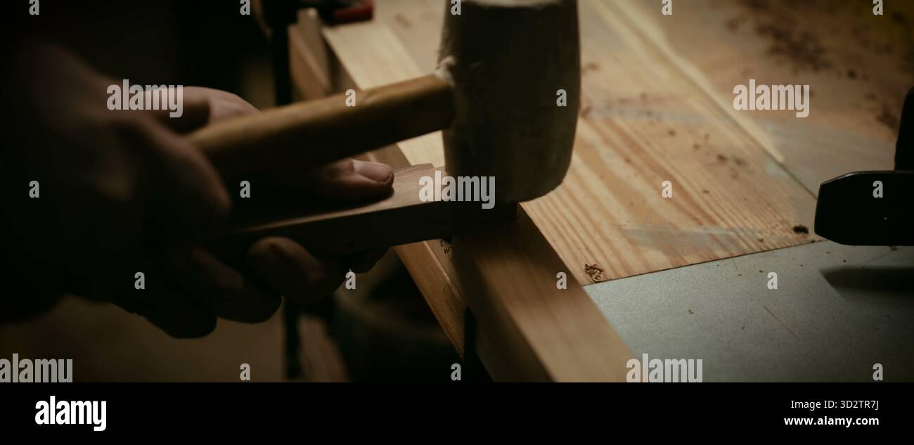 La main d'une personne tapote doucement une cheville en bois en place à l'aide d'un maillet Banque D'Images