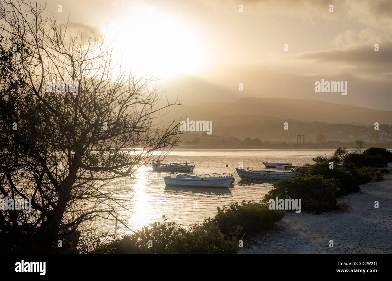 Petits bateaux de pêche amarrés sur les eaux peu profondes d'un canal marin à l'aube avec le soleil d'automne projetant des reflets lumineux sur l'eau calme. Banque D'Images
