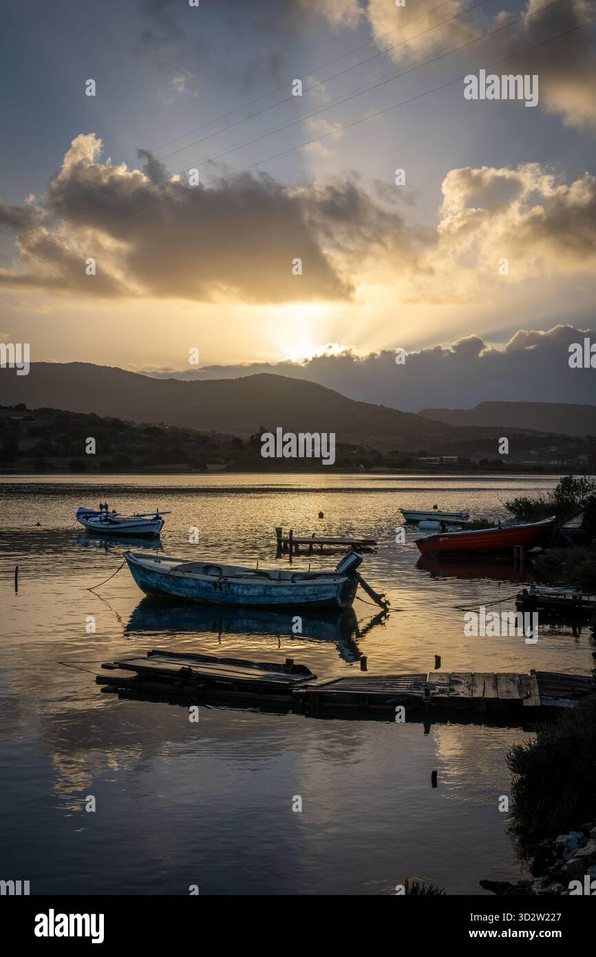 Petits bateaux de pêche en bois amarrés sur un canal marin peu profond à l'aube, avec le soleil d'automne se levant au-dessus des collines projetant une belle lumière du soleil et des nuages Banque D'Images