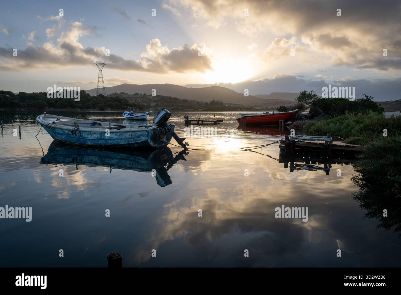 Petits bateaux de pêche en bois amarrés sur un canal marin peu profond à l'aube, avec le soleil d'automne se levant au-dessus des collines projetant une belle lumière du soleil et des nuages Banque D'Images