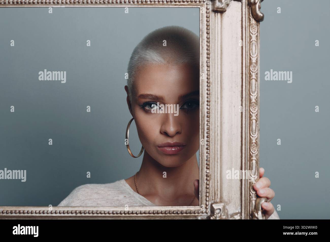 Jeune femme millénaire aux cheveux blonds courts tient le cadre doré dans les mains derrière son portrait du visage Banque D'Images
