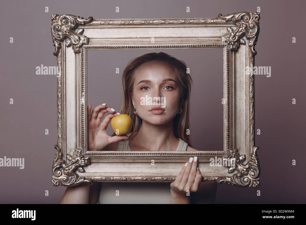 Jeune femme millénial cheveux blonds tient image dorée cadre dans les mains visage portrait avec pomme Banque D'Images