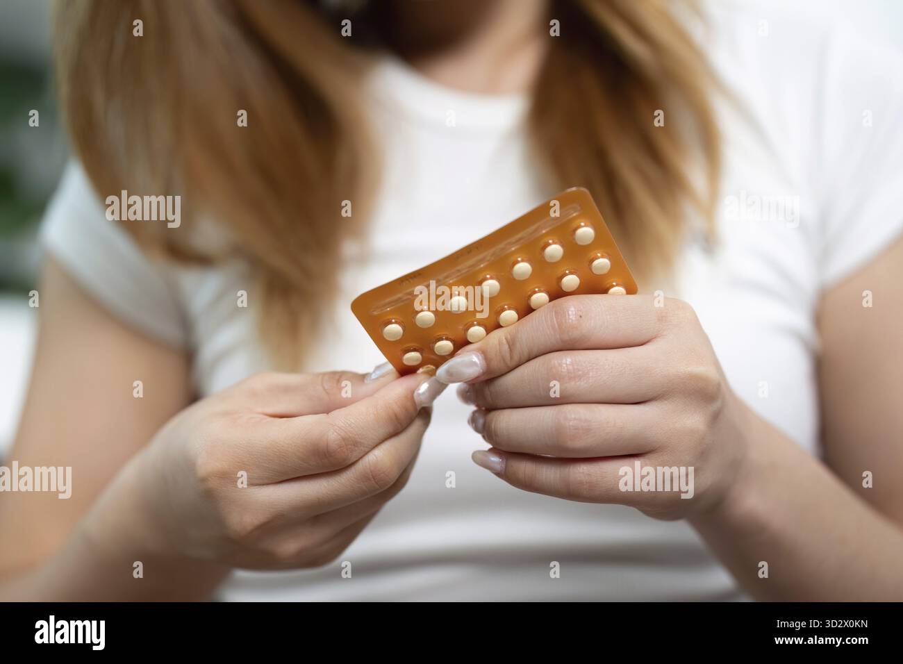 Une femme retire soigneusement une pilule contraceptive d'une plaquette thermoformée, mettant l'accent sur la santé et les soins personnels Banque D'Images