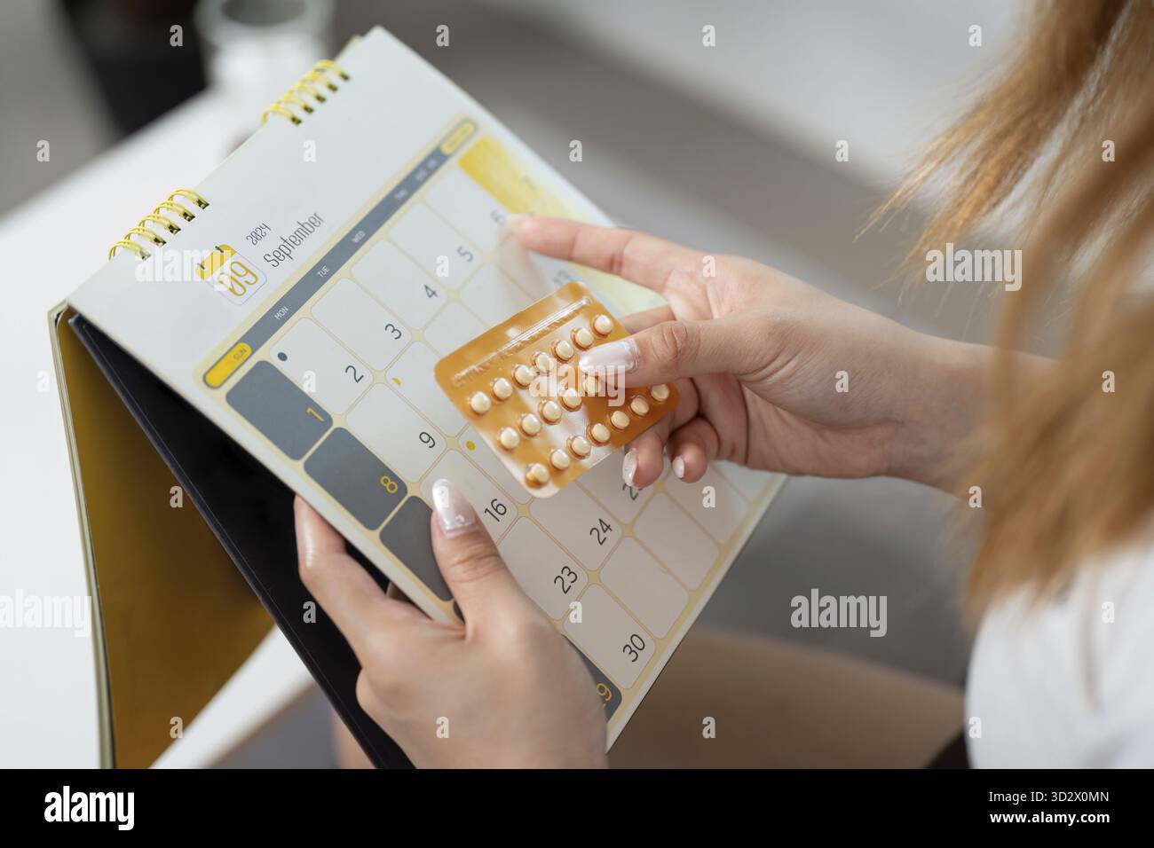 Une femme utilise un calendrier pour suivre sa consommation de pilules contraceptives, soulignant la gestion de la santé et la responsabilité personnelle Banque D'Images
