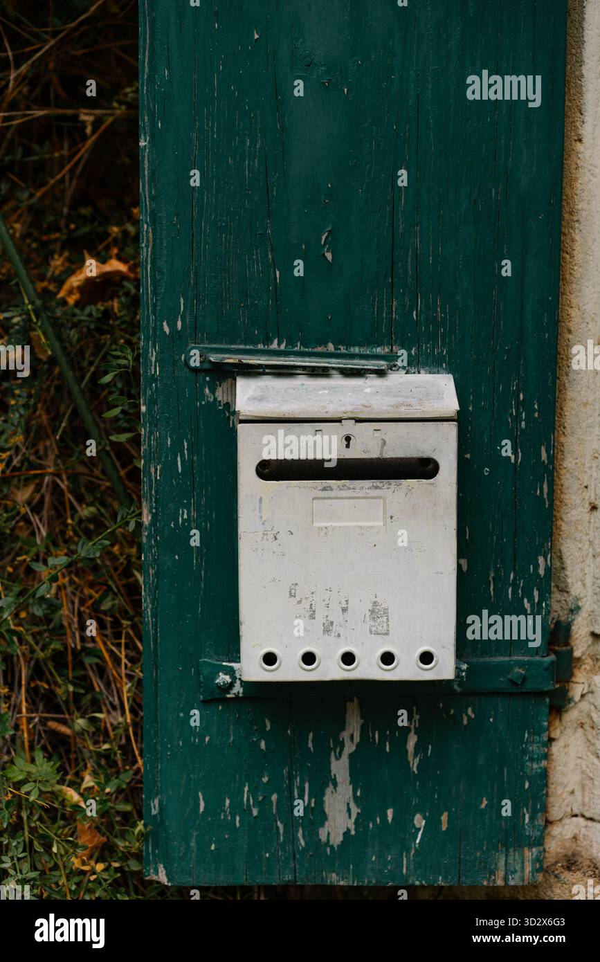 Boîte aux lettres blanche vieillie montée sur une porte en bois vert foncé vieilli avec peinture pelable. Un charmant détail rustique capturant le caractère d'un ancien euro Banque D'Images
