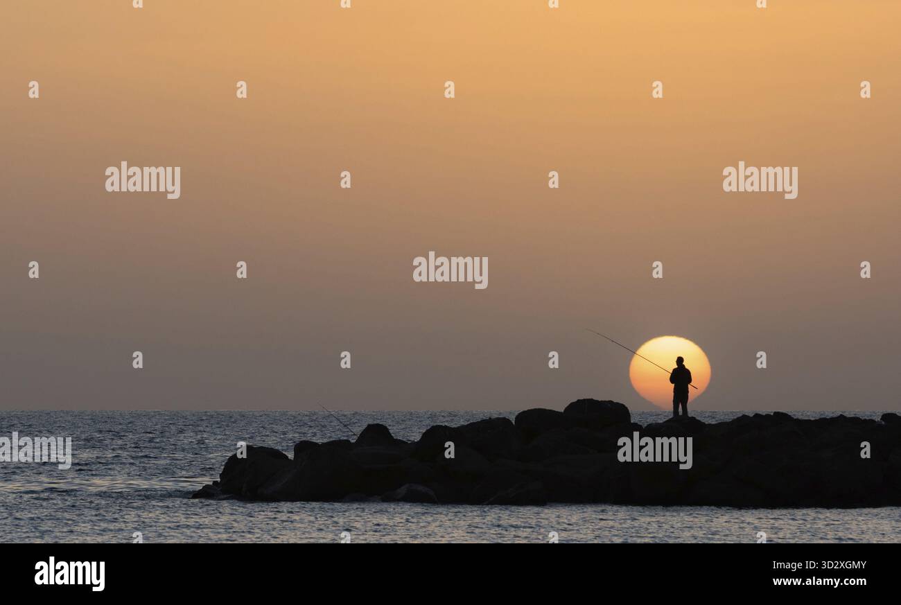 Silhouette sous le soleil bas d'un homme pêchant sur la plage d'Amadores sur l'île de Gran Canaria en Espagne Banque D'Images