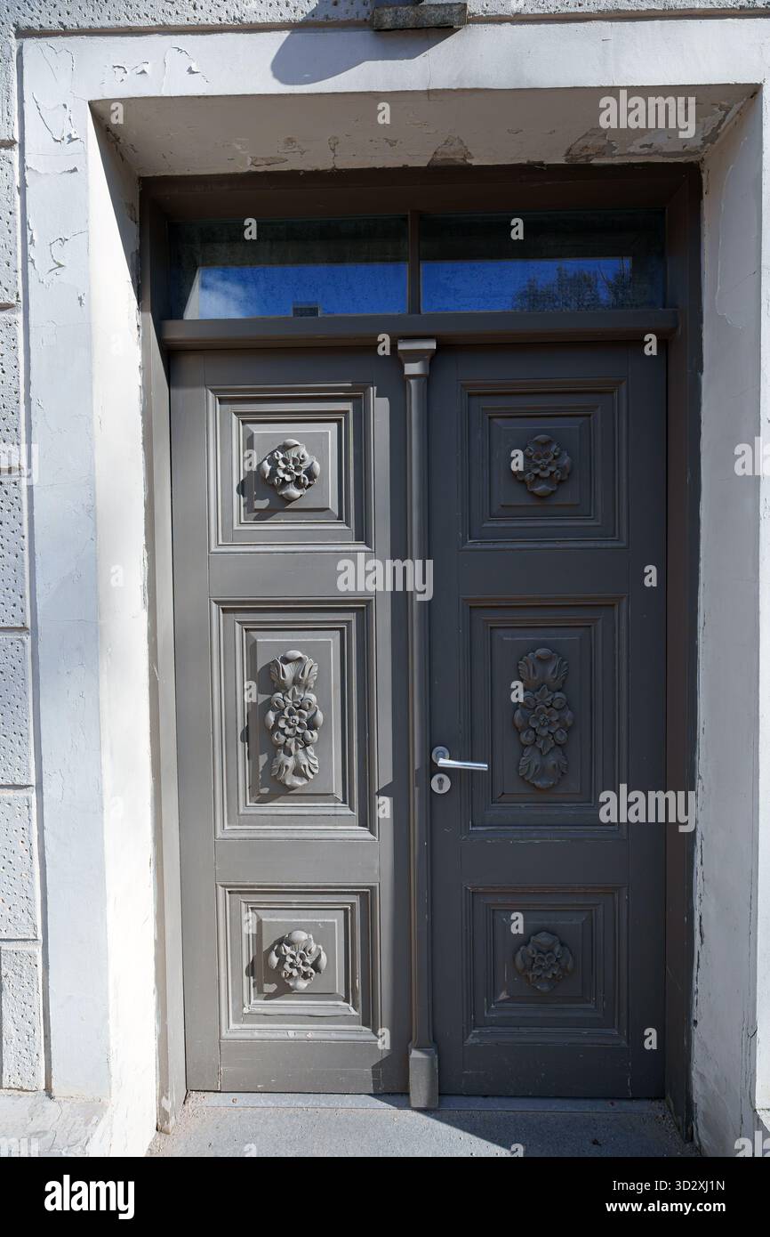 Un gros plan vertical d'une double porte en bois gris bien entretenue avec d'élégantes sculptures florales et des panneaux surélevés, placé dans une porte en pierre blanche de Banque D'Images