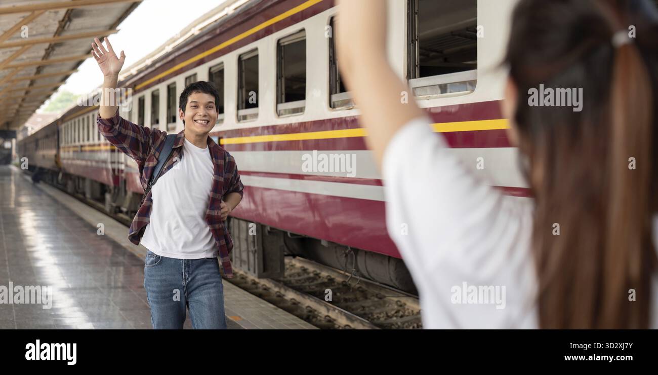 Un homme fait signe au revoir à son partenaire à la gare, incarnant l'excitation et l'émotion alors qu'ils commencent leur voyage Banque D'Images